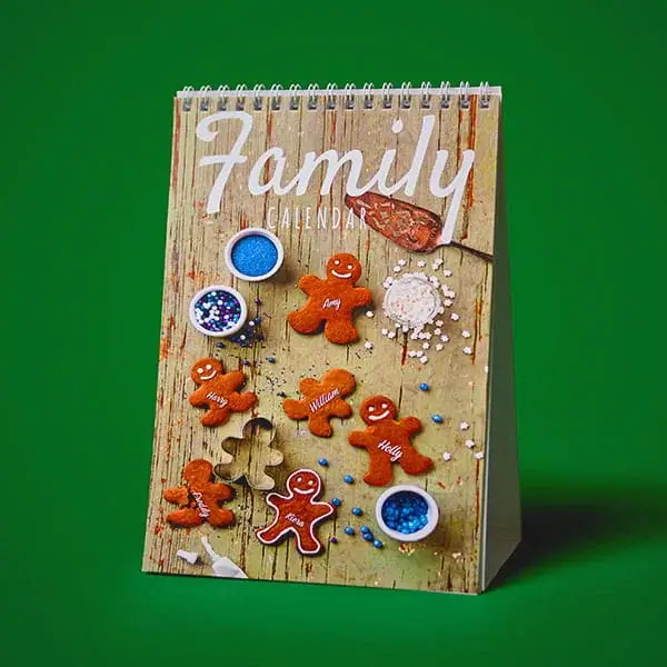 Christmas family desk calendar featuring gingerbread biscuits, baking ingredients, and festive decorations on a rustic wooden background.